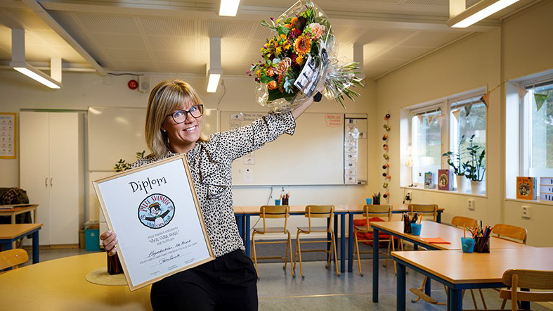 Förstelärare Ida Prisell poserar glatt med diplom och blombukett i ett klassrum