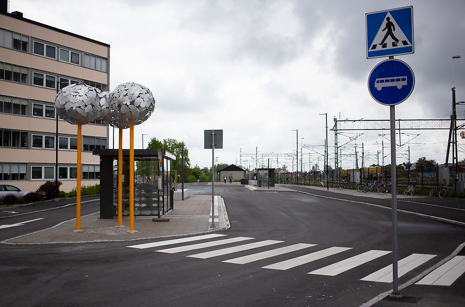 Vy över stationsområdet i Åstorp - konstverket trillingnöten och en busskur.